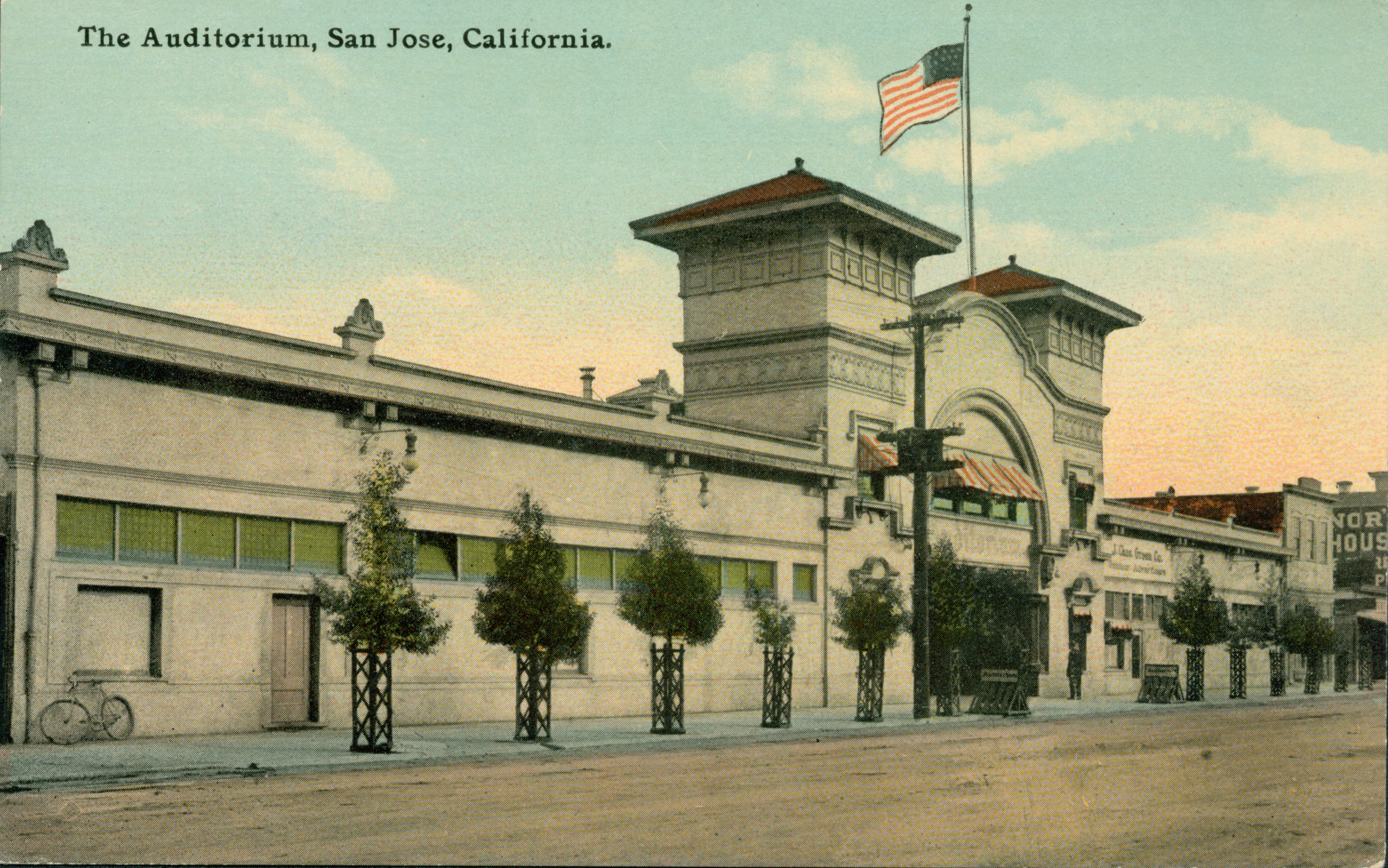 Exterior view of Auditorium Pavilion, small tree lined street with flag on top of building