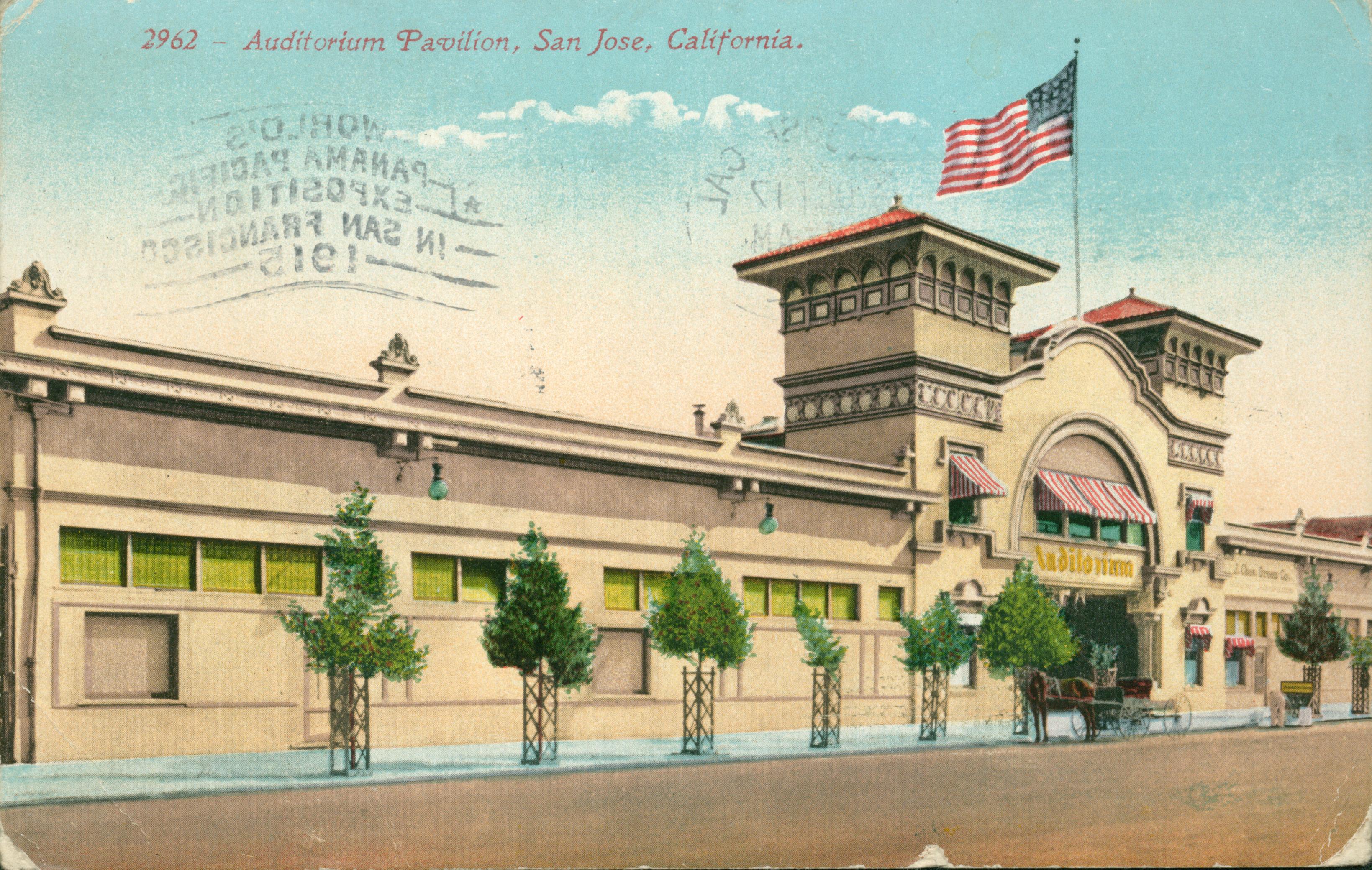 Exterior view of Auditorium Pavilion, small tree lined street with flag on top of building