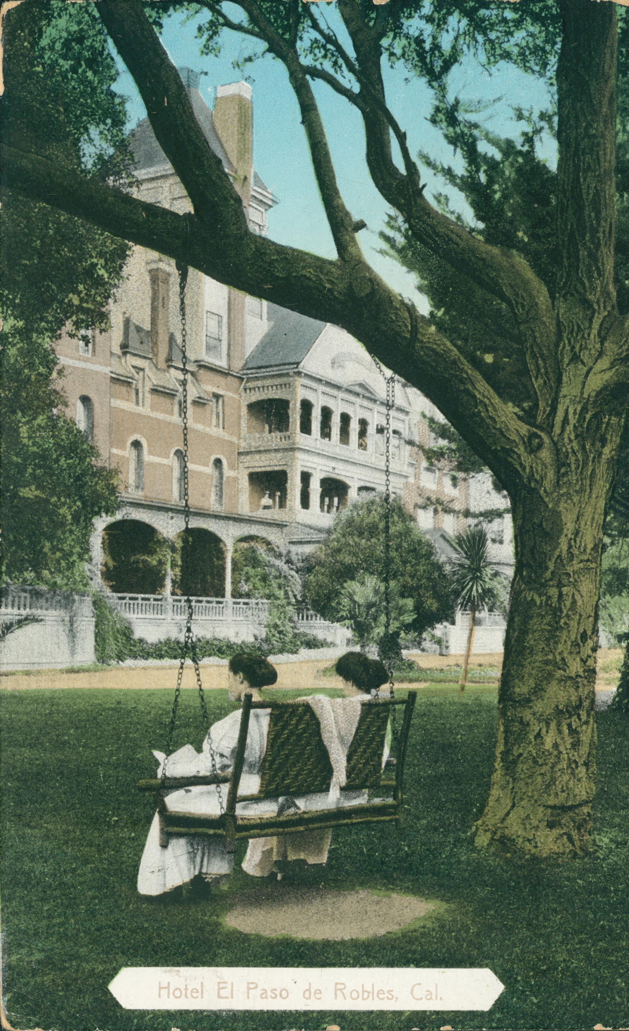 Hotel in the background, two ladies rocking in a tree swing hanging from a large tree