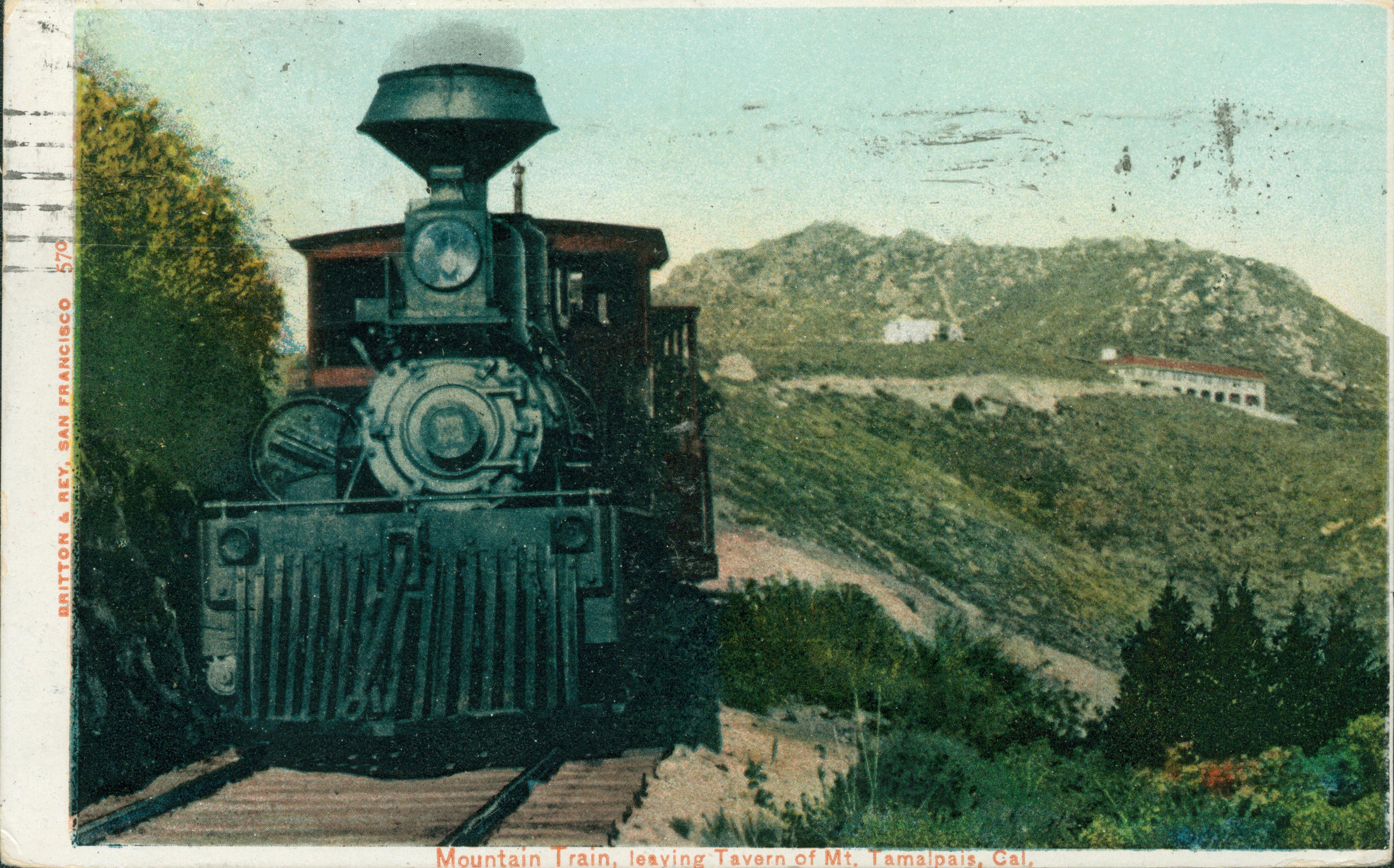 Steam engine traveling on track, building in background, mountains and hills, with shrubbery in background