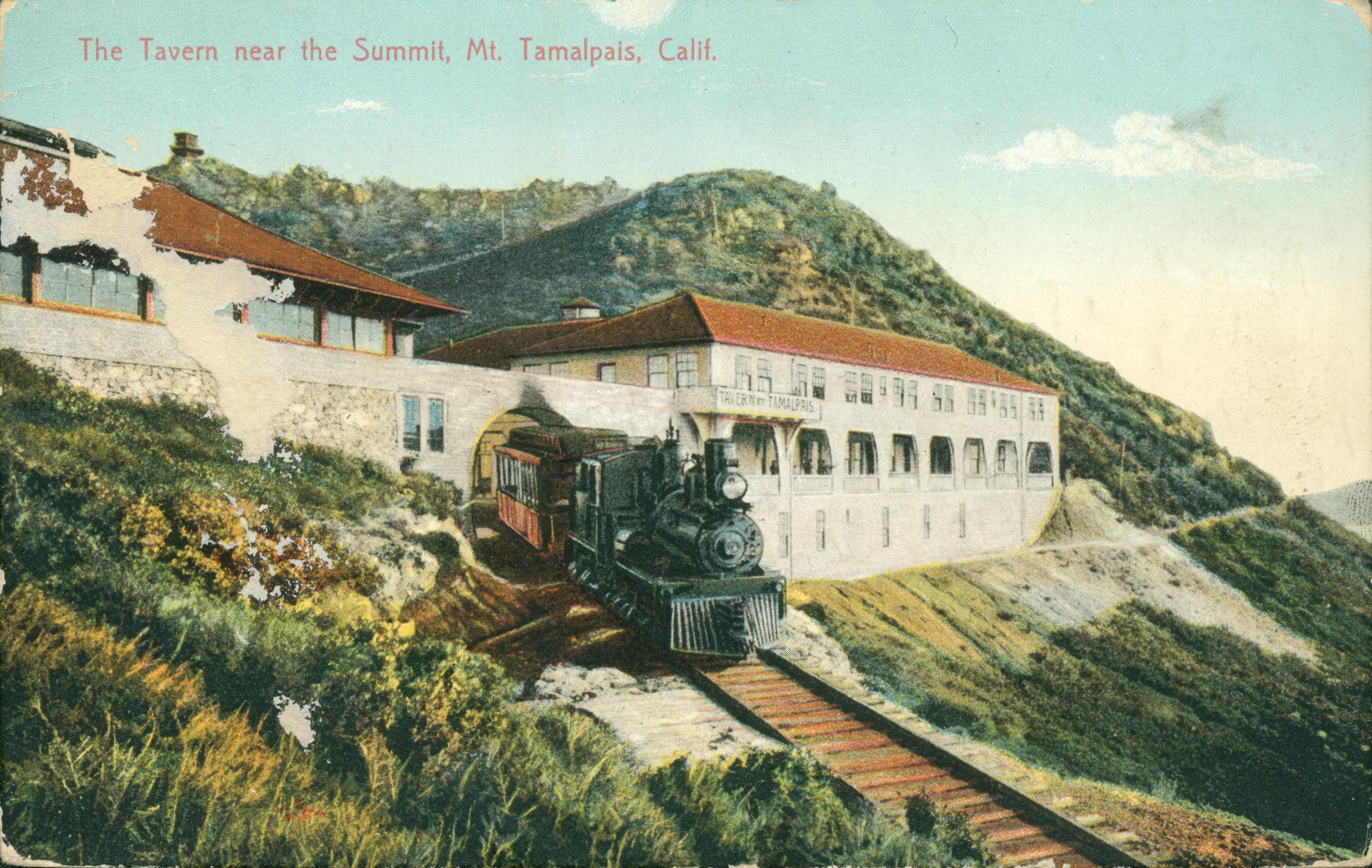 View of Mt. Tamalpais, trees, hills and buildings in background, train and train tracks in foreground