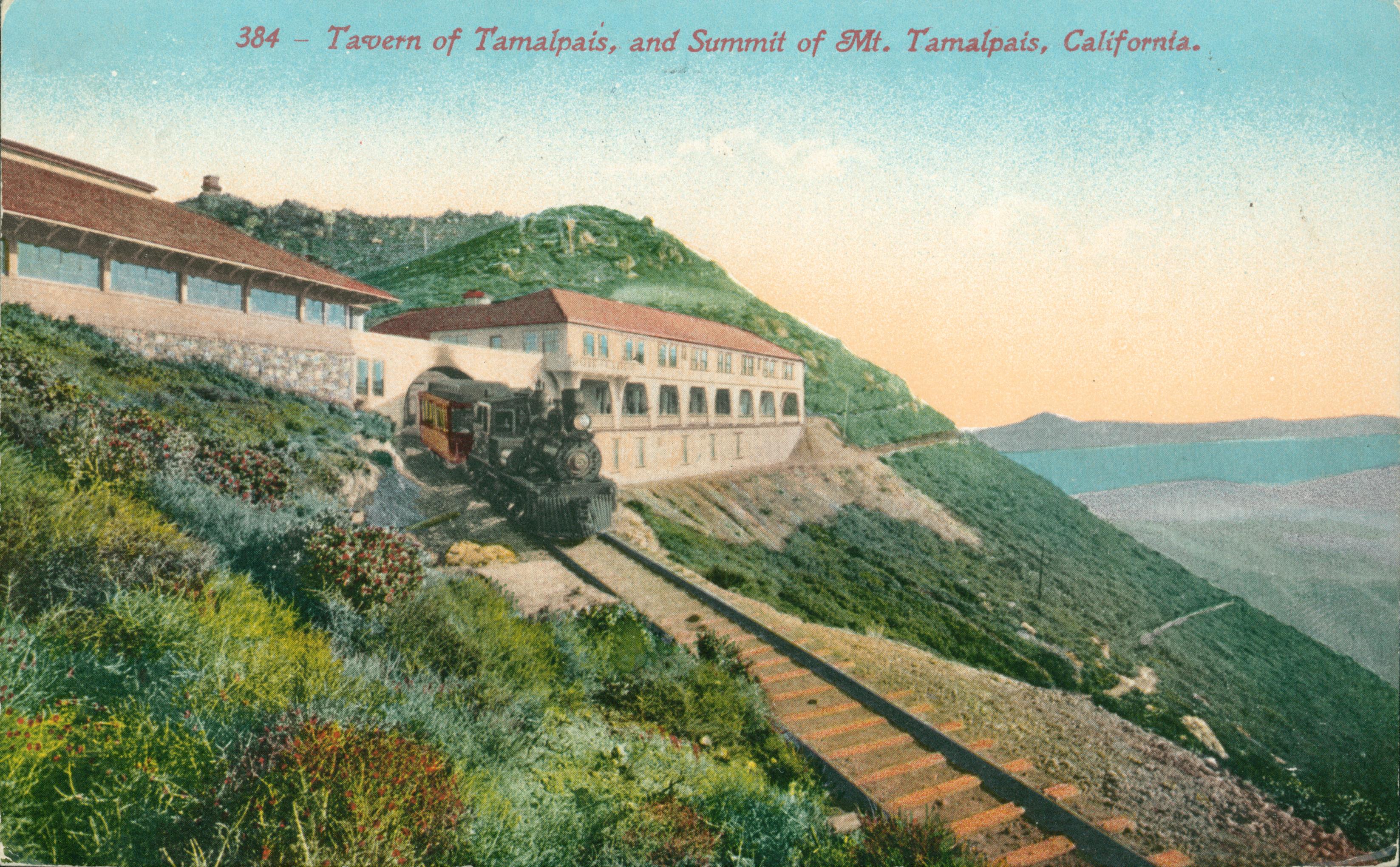 View of Mt. Tamalpais, trees, hills and buildings in background, train and train tracks in foreground