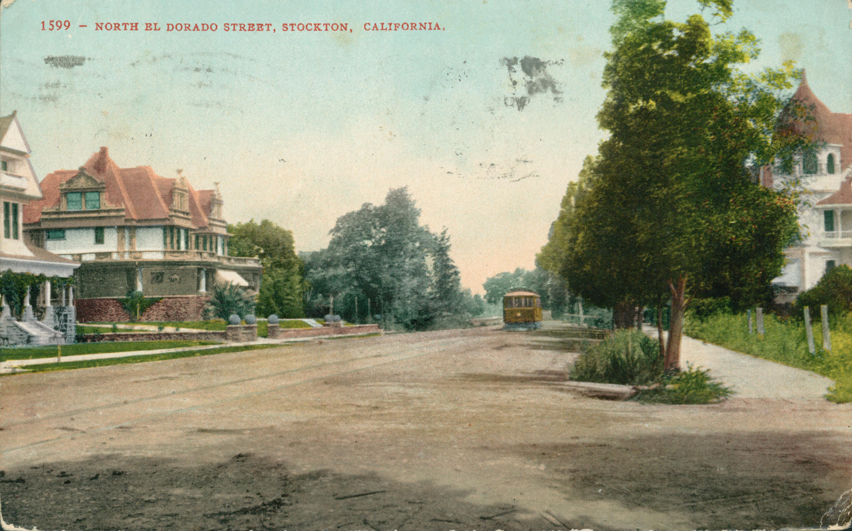 View of North El Dorado Street, dirt road with a trolley and tracks down the center, large houses on either side of the street with trees in between the street and the houses