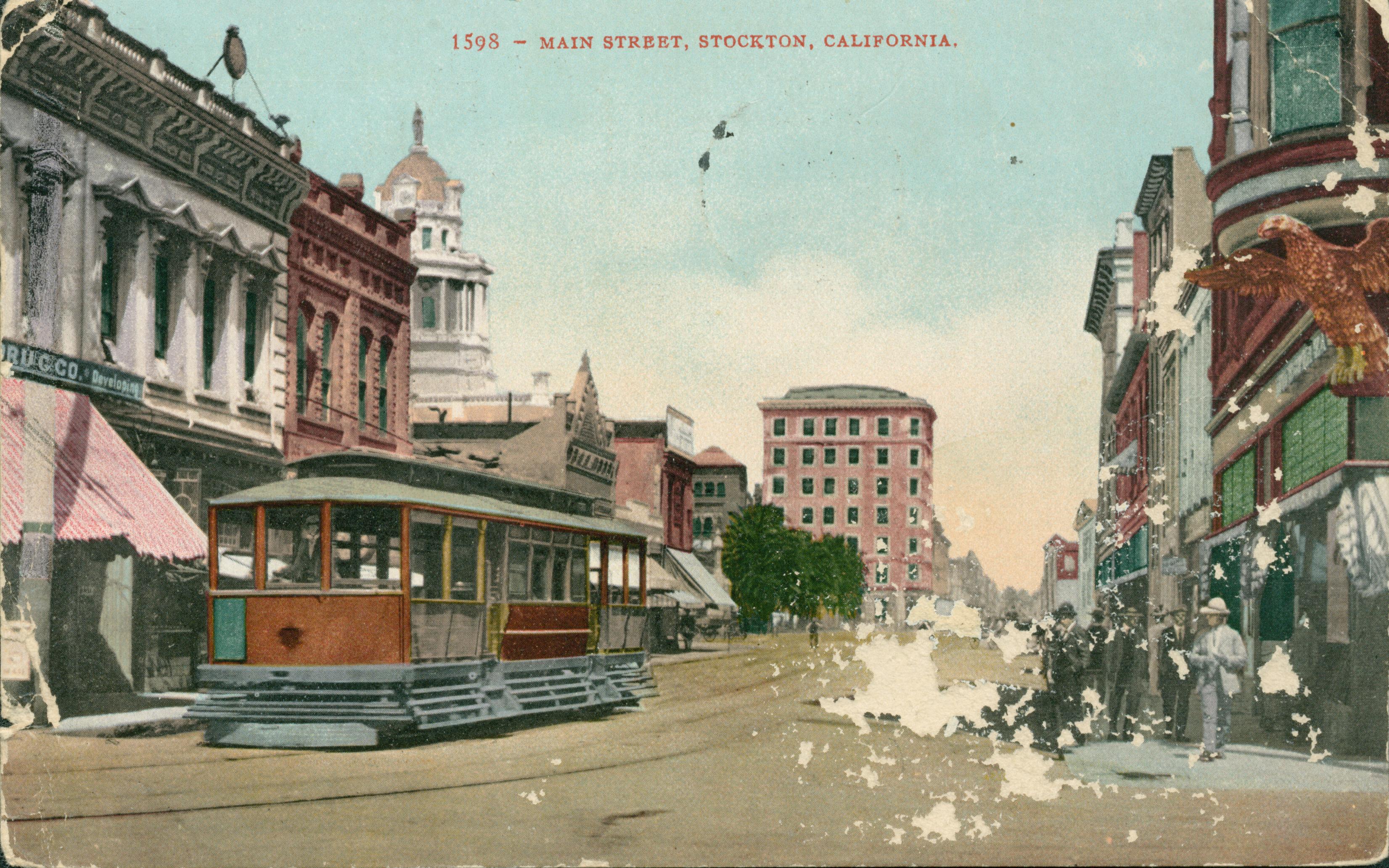 View of Main Street with trolley car and tracks down the center of the street, people waiting on corner