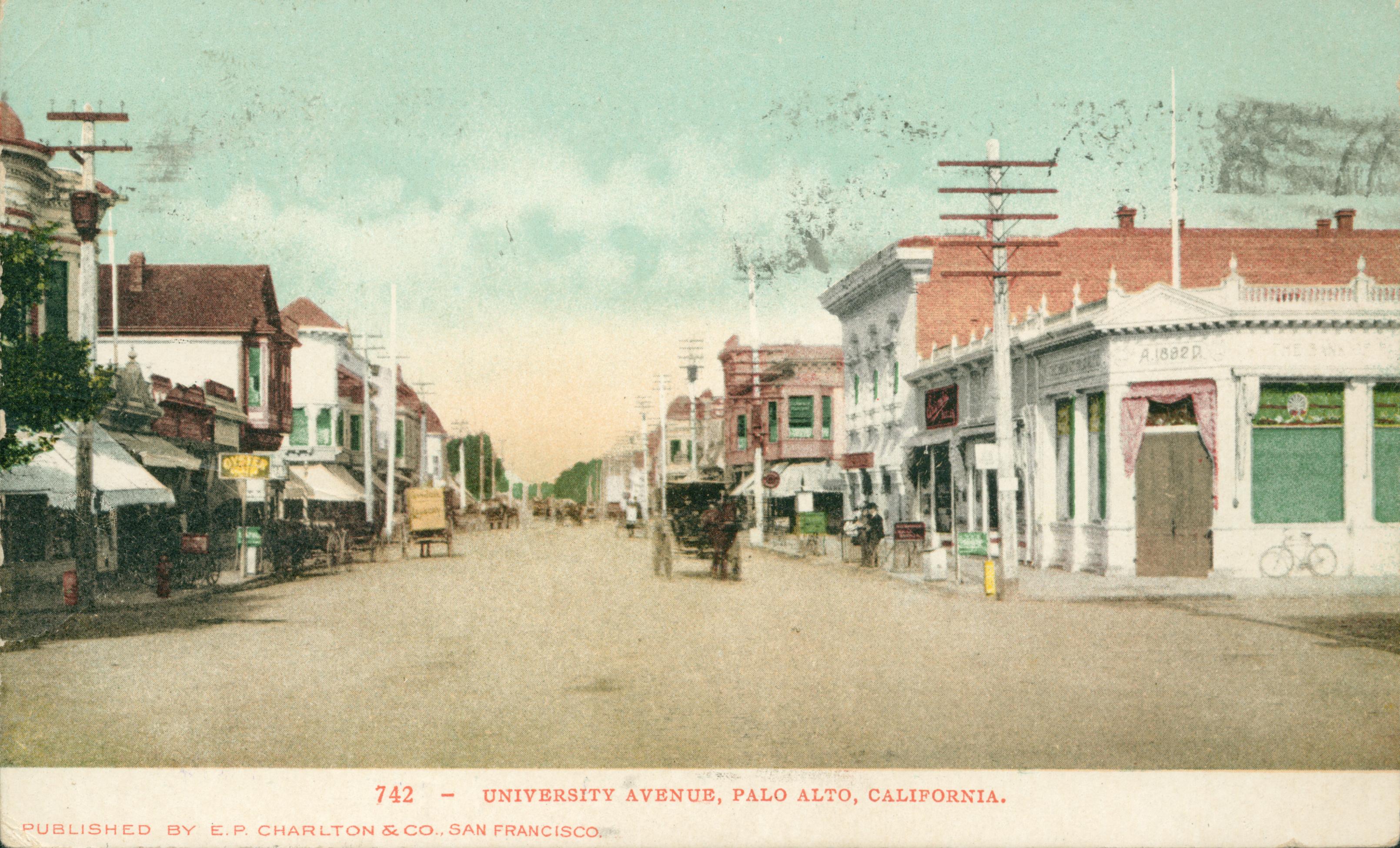 View of University Ave., buildings bordering the dirt road, electricity poles bordering the road on both sides, horse-drawn carriages traveling down the road