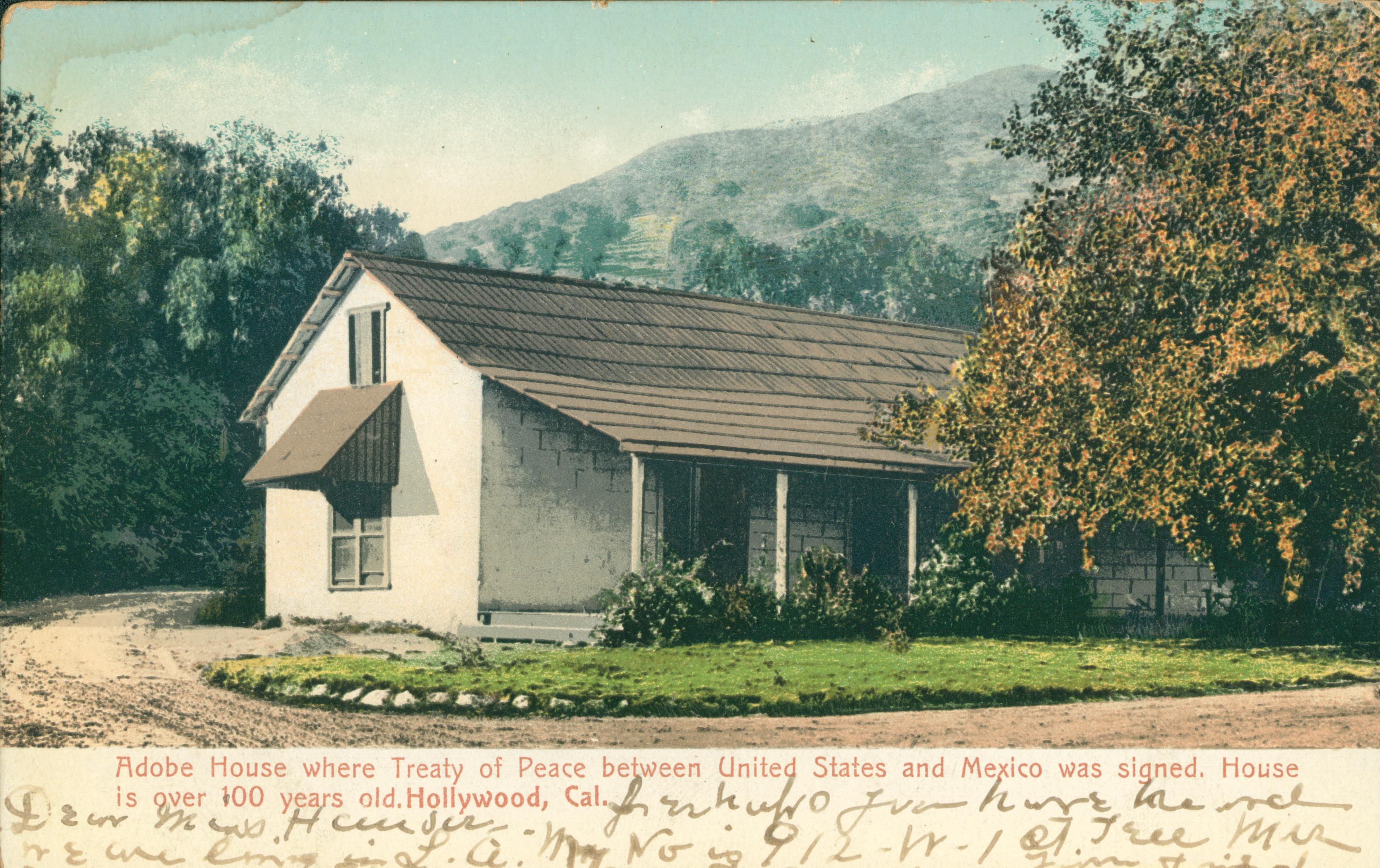This postcard shows an Adobe house facing a dirt road.