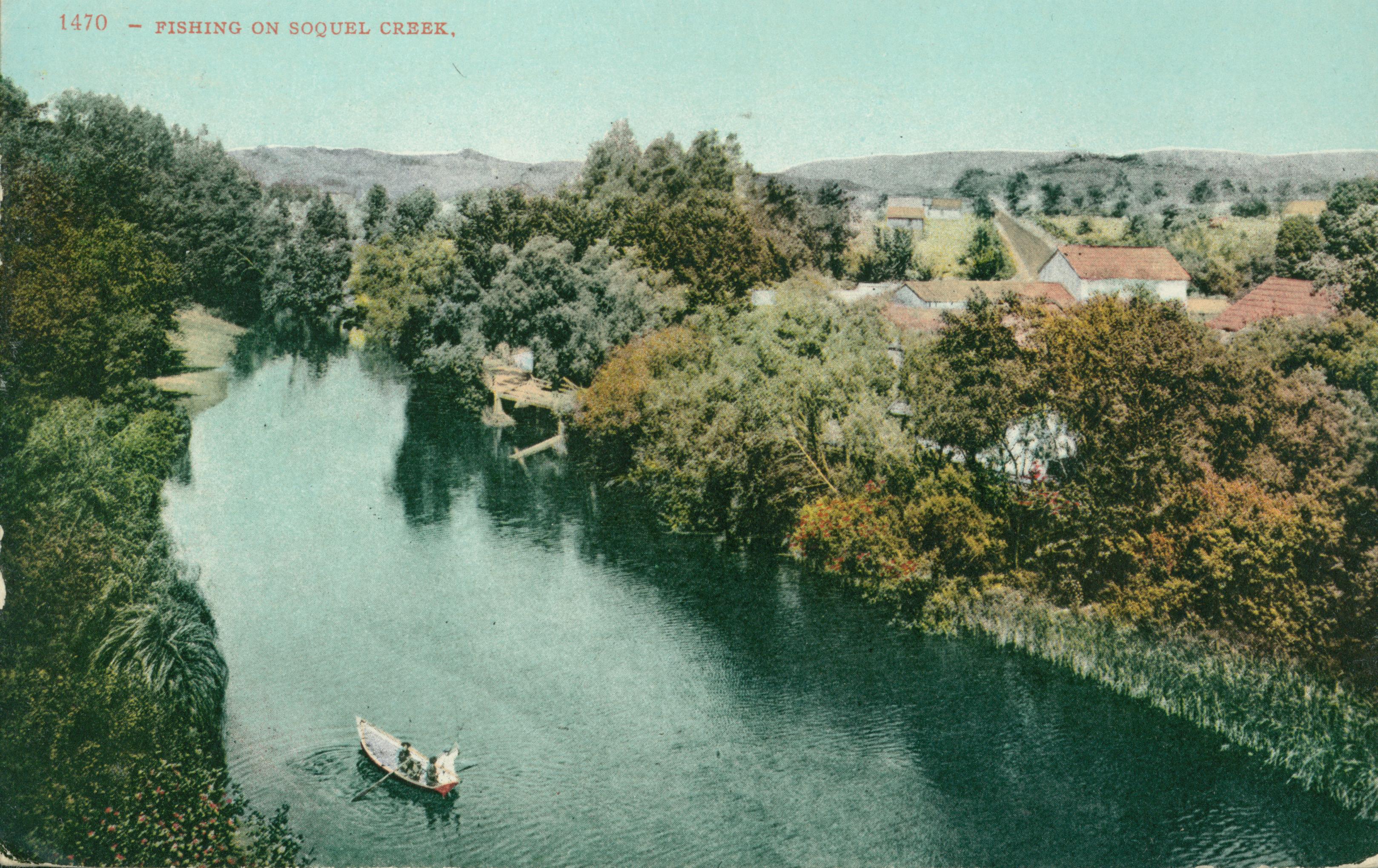 People in a canoe-like boat fishing on the river/creek surrounded by trees and bushes, buildings near the banks of the river/creek