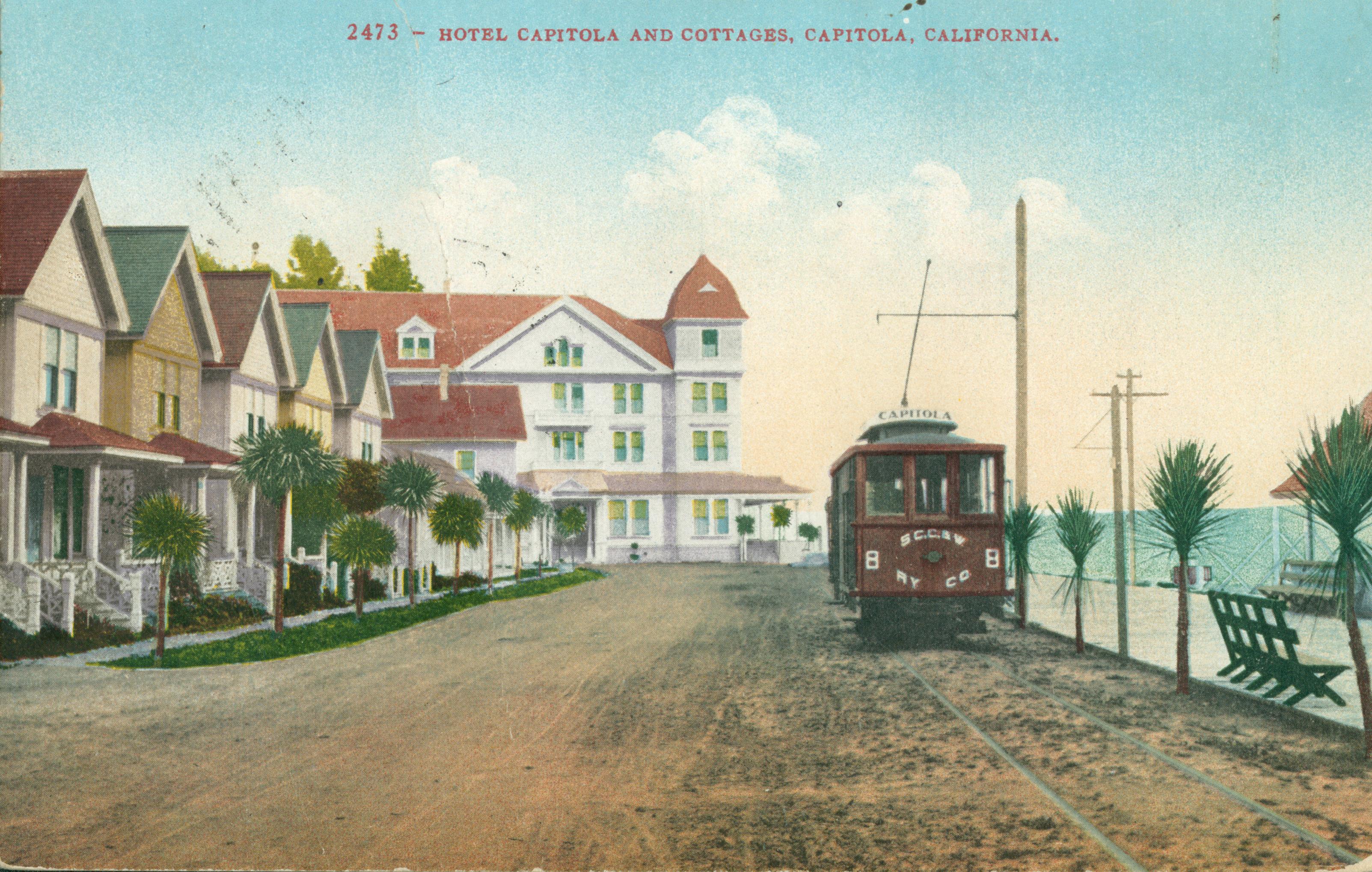 Exterior views of cottages and Hotel Capitola, dirt drive with electric trolley parallel to ocean front walk with benches and palm trees, ocean view