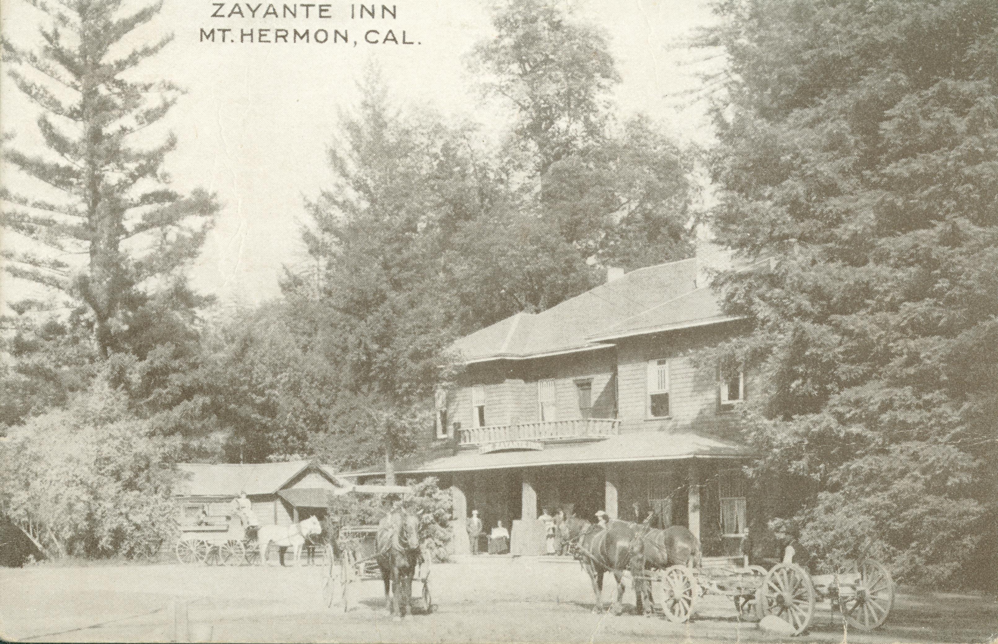 Horse and wagons stand on a path in front of the Zayanta Inn, people are standing and sitting on the porch of the inn, surrounded by trees and large open area in front