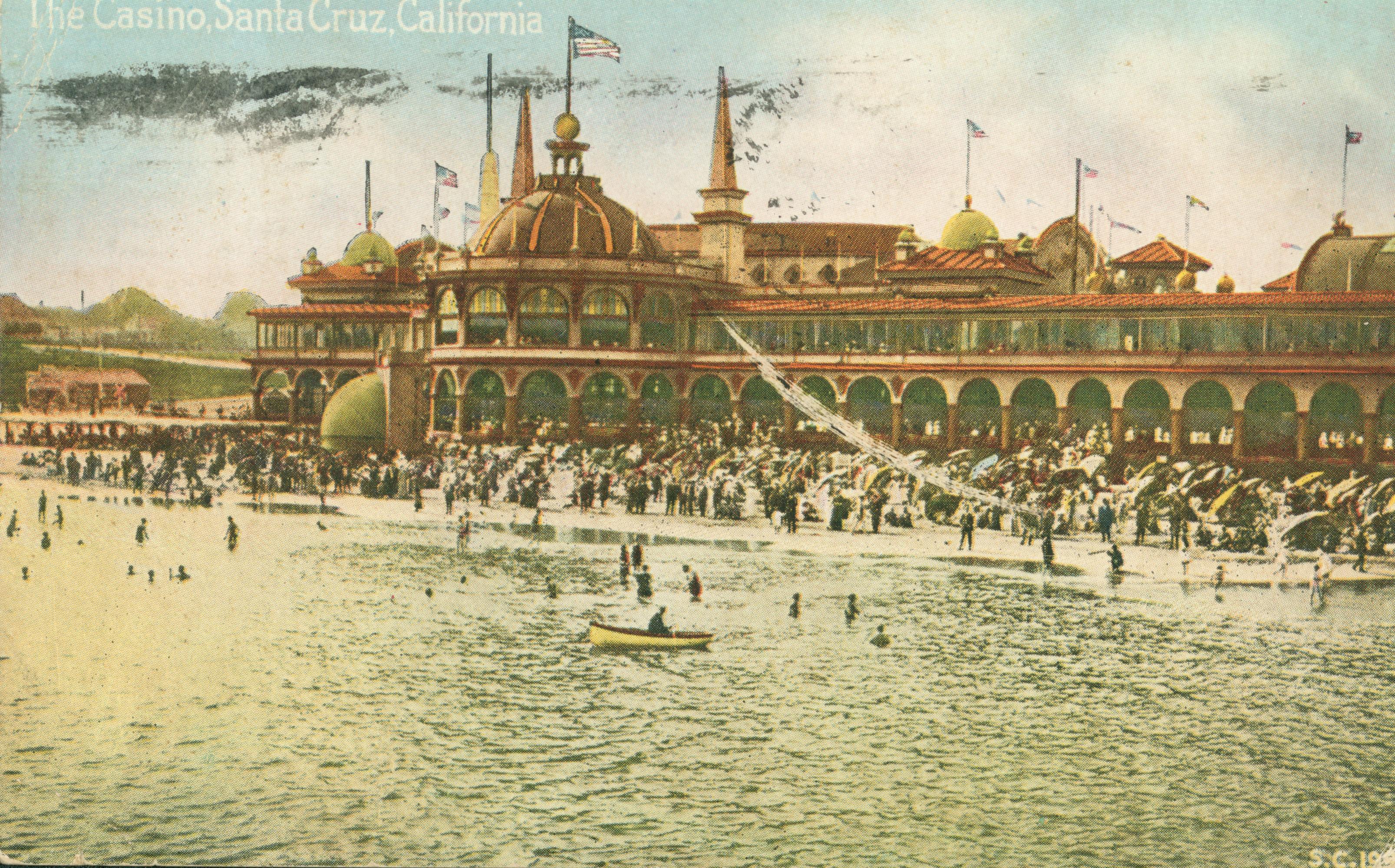 View of people sitting on the beach and swimming in ocean, in front of the casino, exterior view of buildings in background,